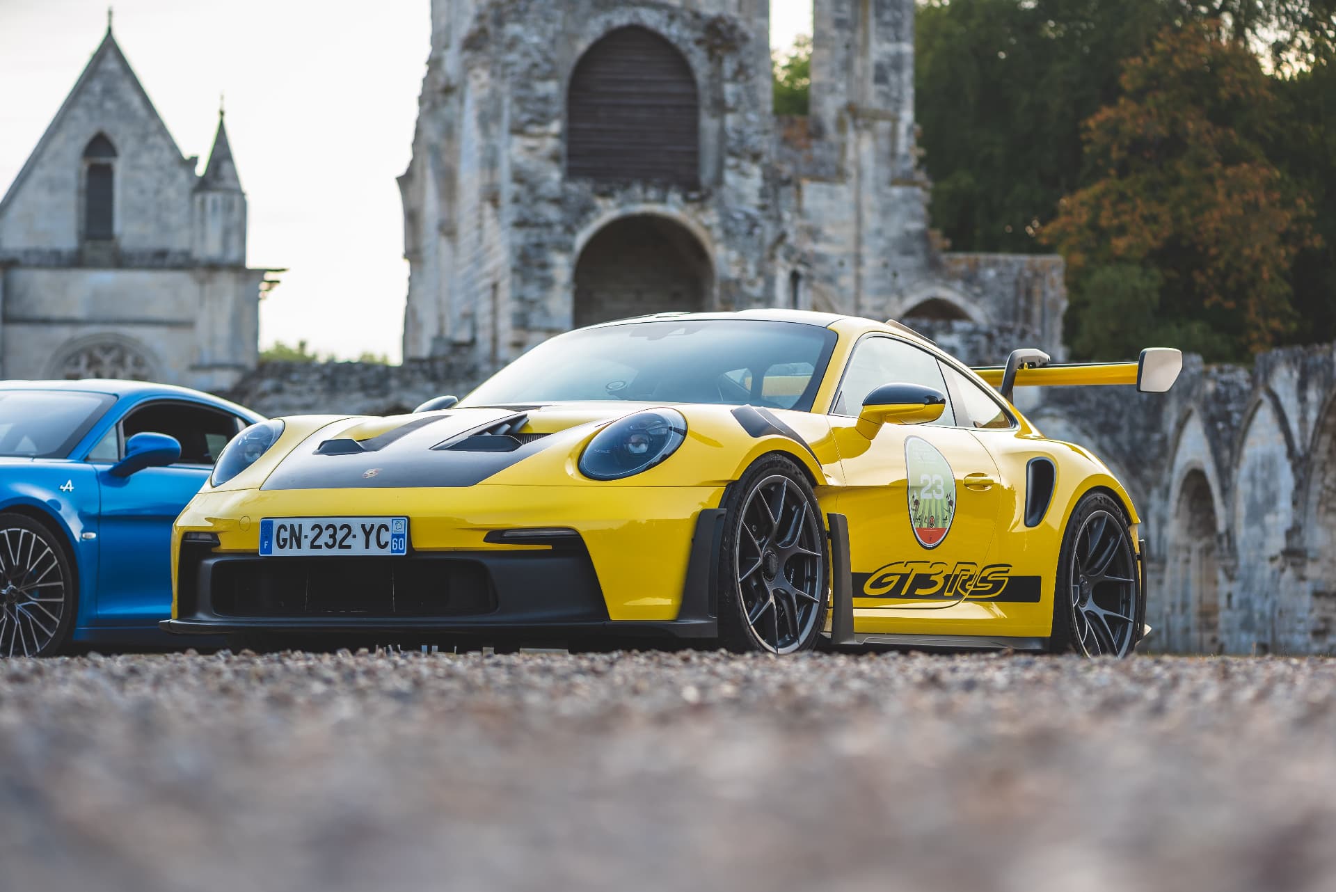 Porsche jaune et Alpine bleue devant une église