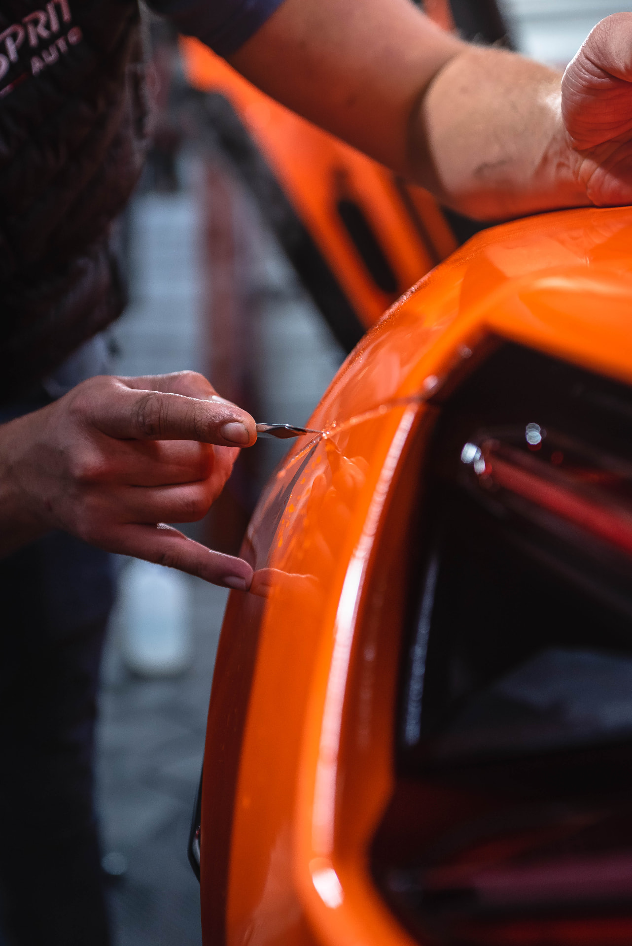 Mains travaillant le film de protection sur l'aile orange d'une Lamborghini