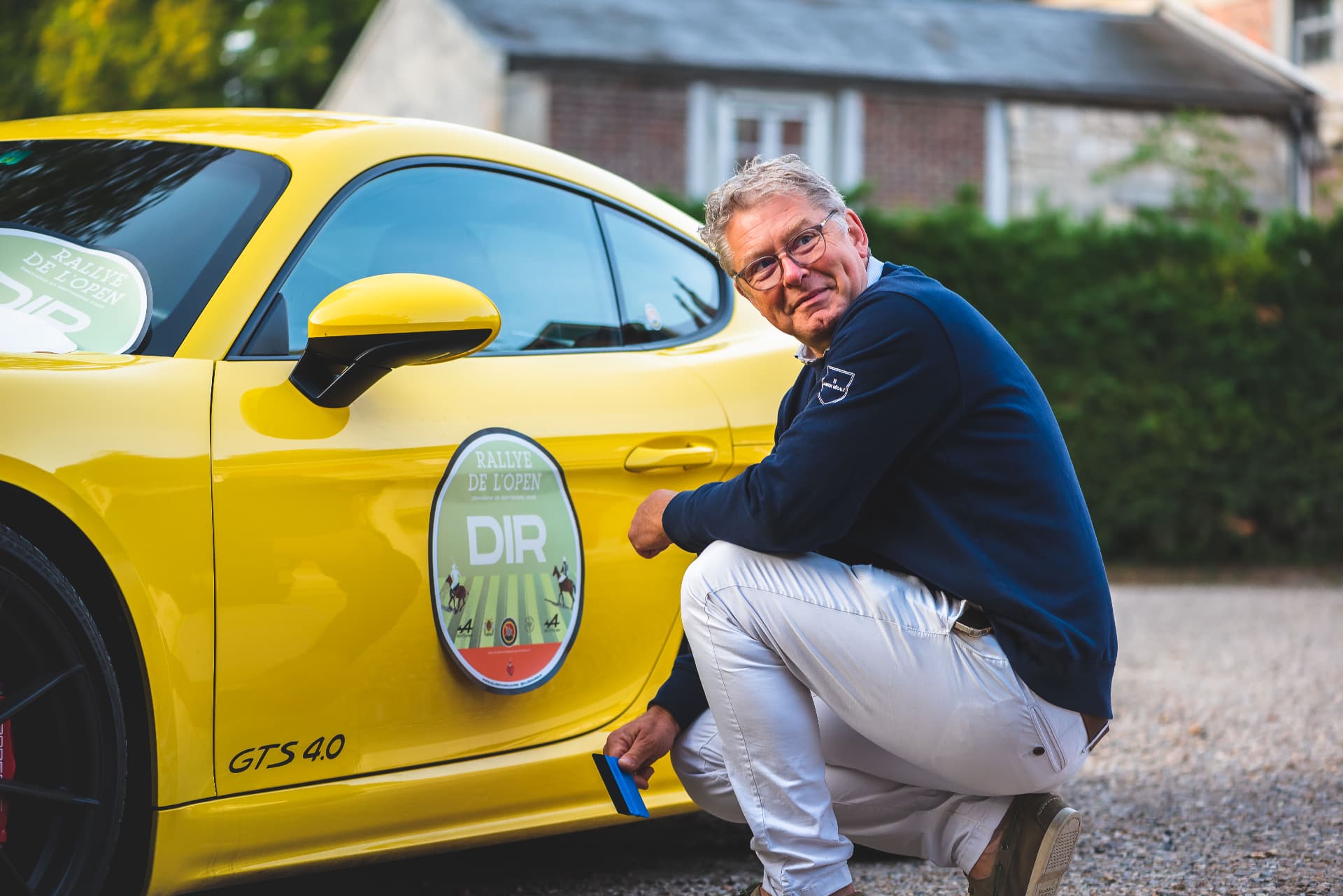 Participant accroupi près d'une Porsche jaune portant la plaque du Rallye de l'Open