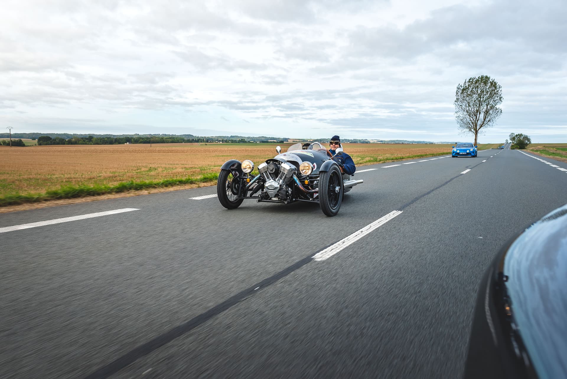 Trois-roues et Alpine bleue sur une route de campagne