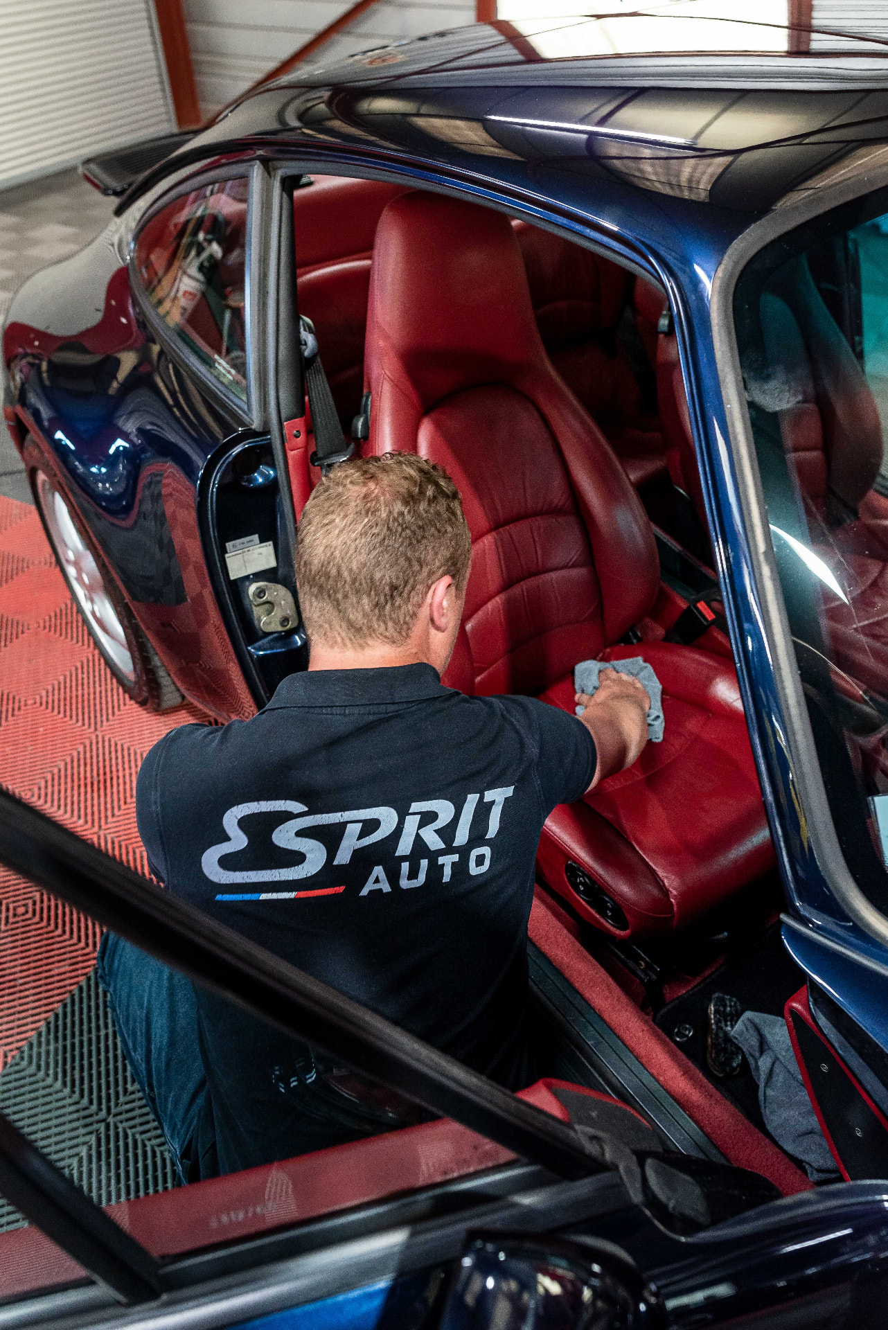 Technicien Esprit Auto intervenant sur l'habitacle en cuir rouge d'une Porsche bleue