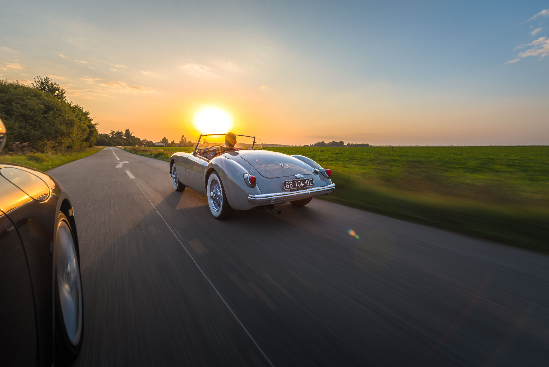 Reportage Esprit Auto — cabriolet roulant sur une route au coucher du soleil