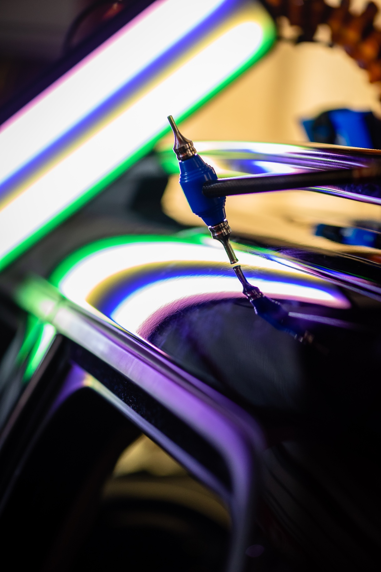 Outil de débosselage posé sur une carrosserie reflétant des néons colorés