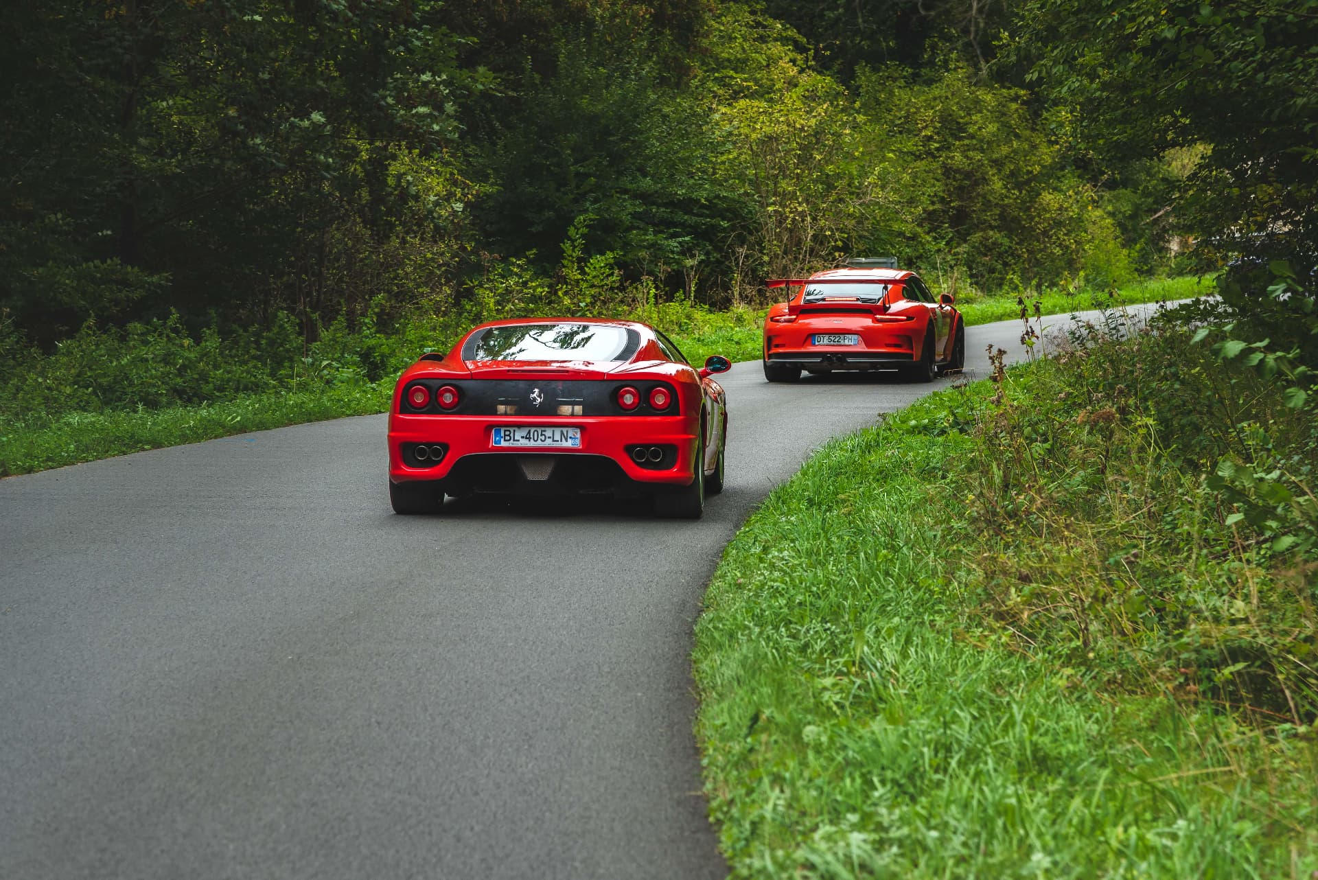 Deux Ferrari rouges dans un virage bordé de verdure, Rallye de l'Open