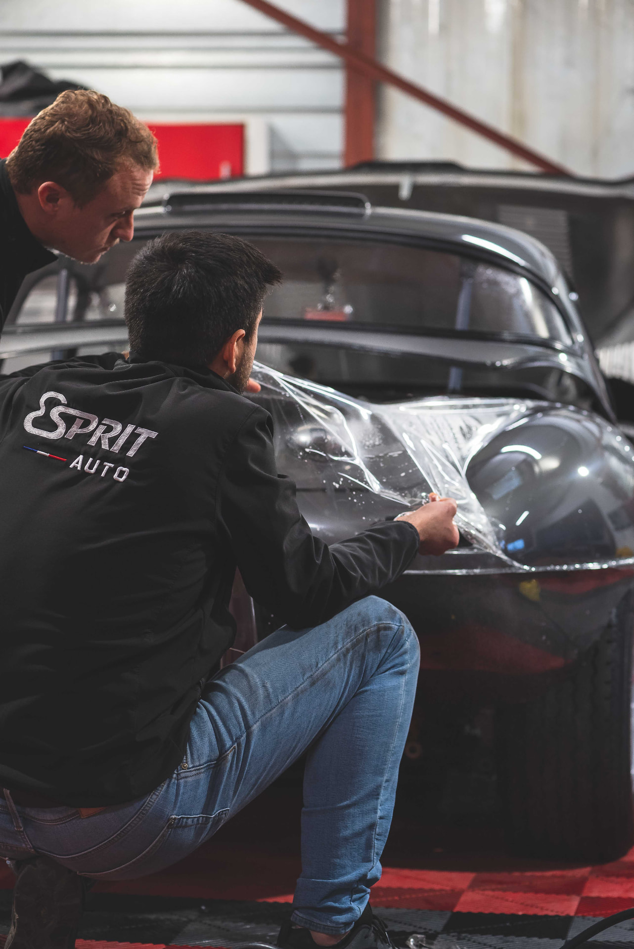 Deux techniciens Esprit Auto posant un film de protection sur un roadster noir