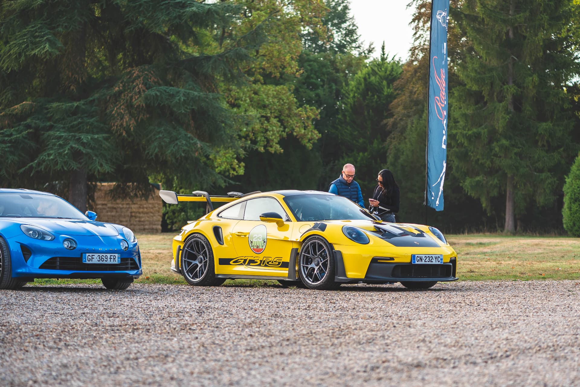 Alpine bleue et Porsche jaune stationnées dans un domaine boisé