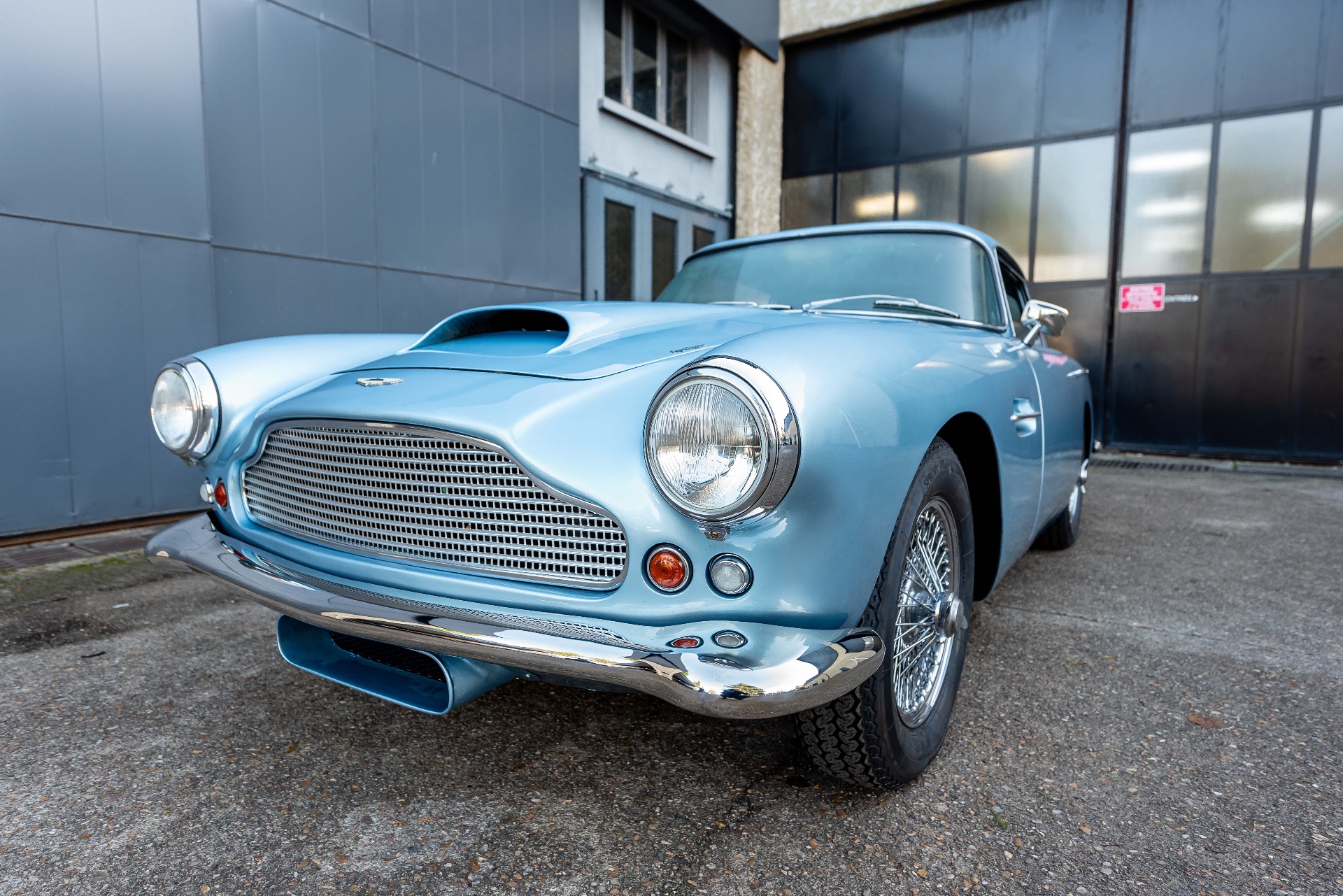 Aston Martin DB4 bleu ciel, vue avant trois-quarts devant un atelier
