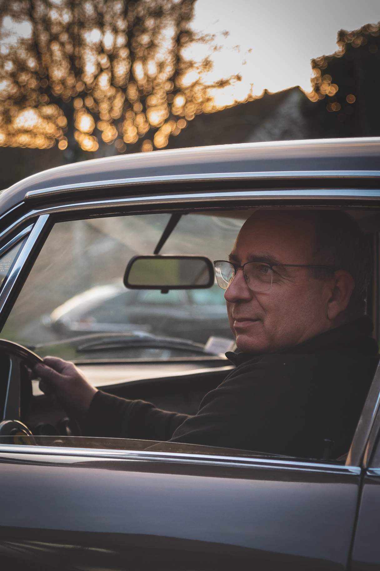Portrait du collectionneur au volant d'une voiture classique, lumière dorée de fin de journée