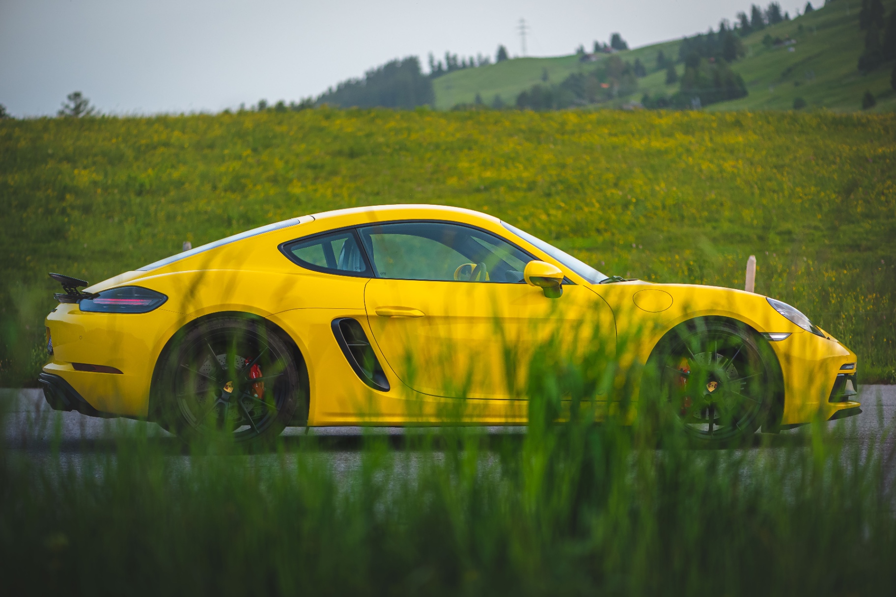 Profil latéral de la Porsche 718 Cayman GTS jaune derrière l'herbe
