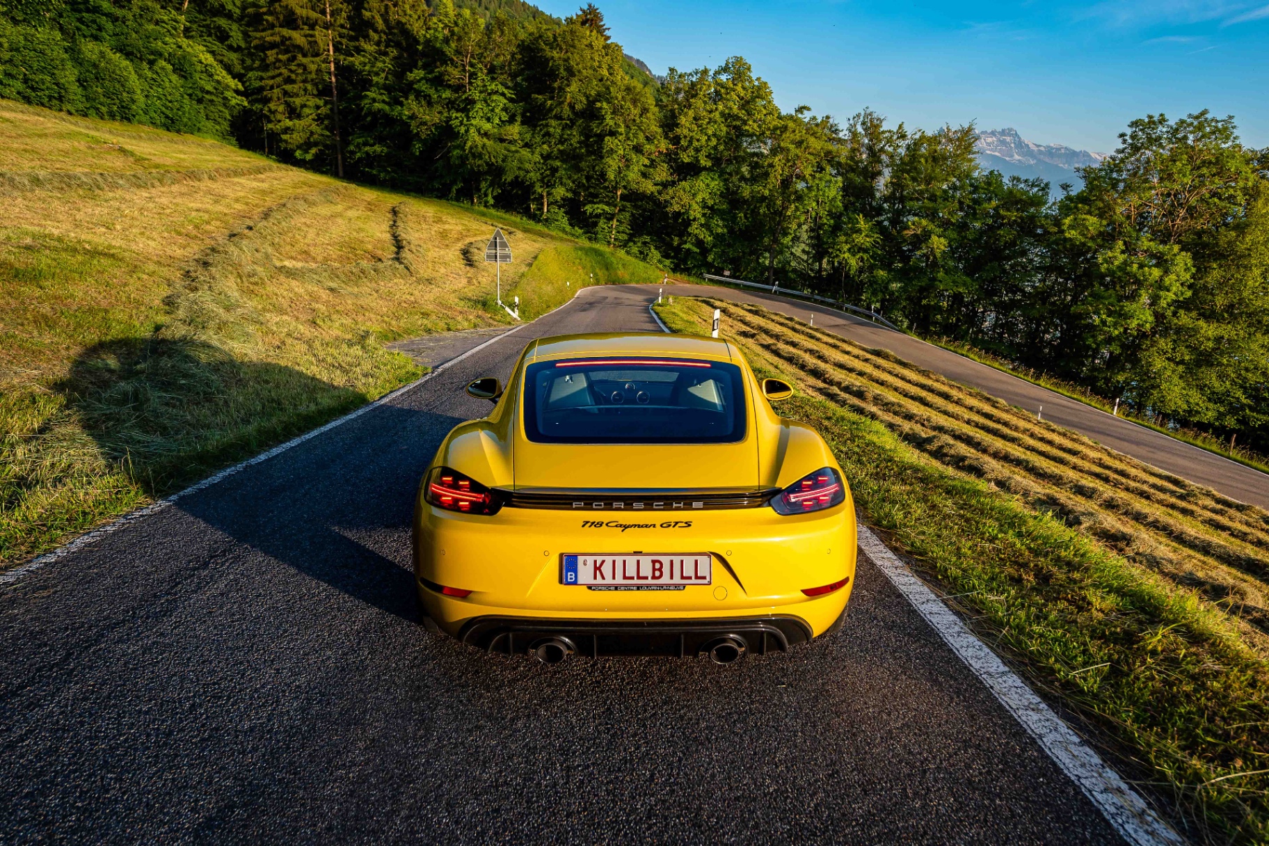 Porsche 718 Cayman GTS jaune vue de l'arrière sur une route sinueuse de montagne