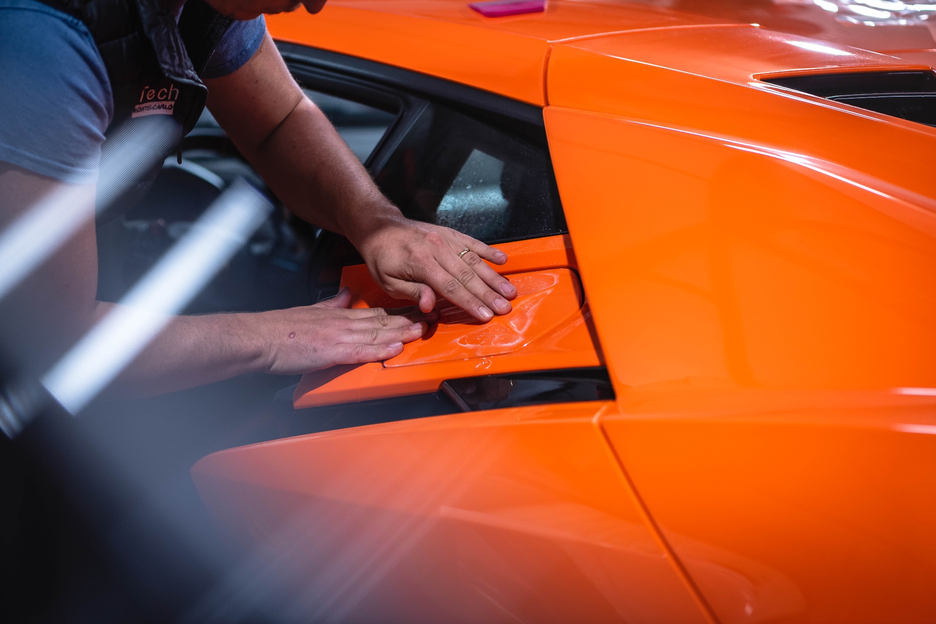 Mains lissant le film PPF sur la carrosserie orange